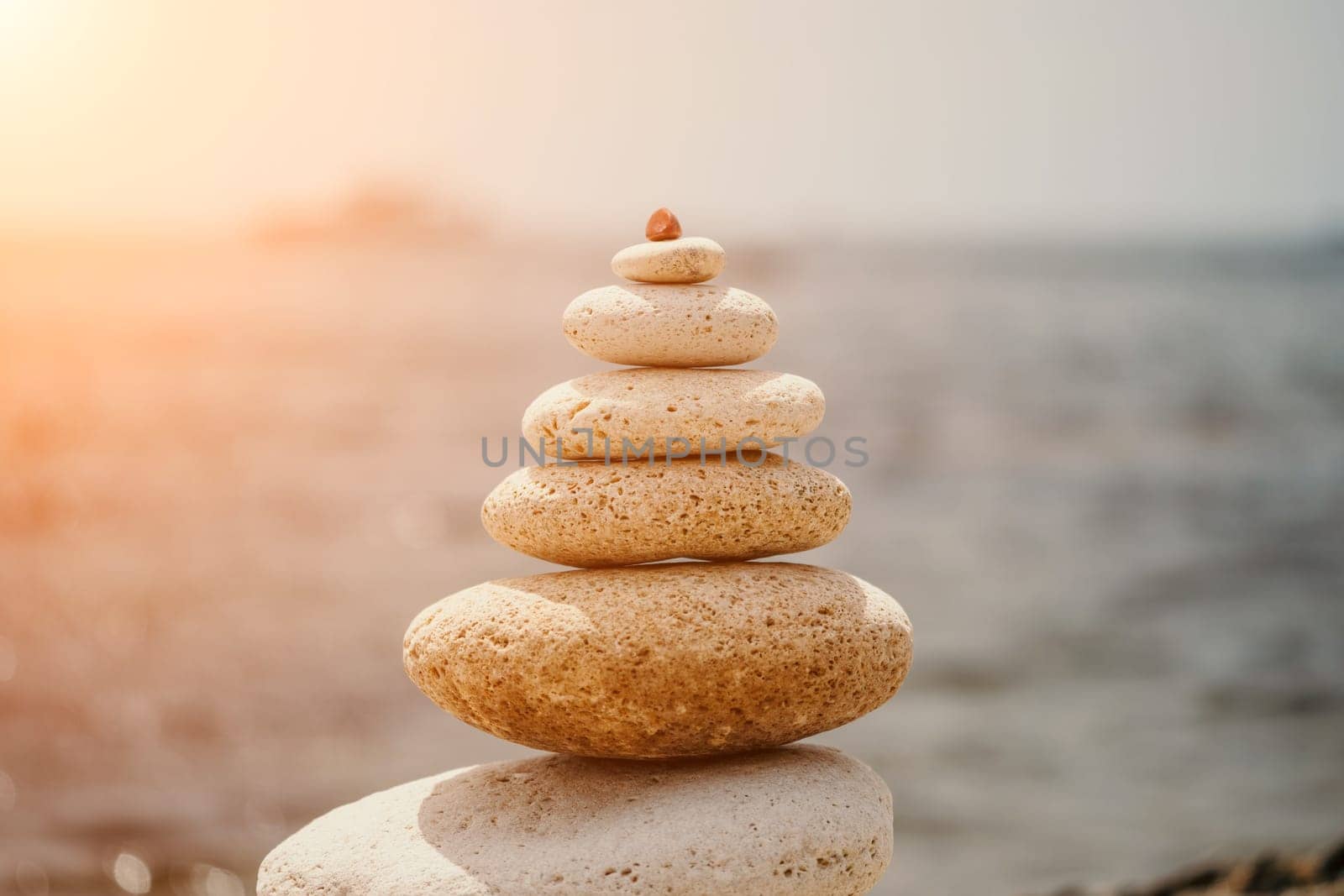 Pyramid stones on the seashore with warm sunset on the sea background. Happy holidays. Pebble beach, calm sea, travel destination. Concept of happy vacation on the sea, meditation, spa, calmness.