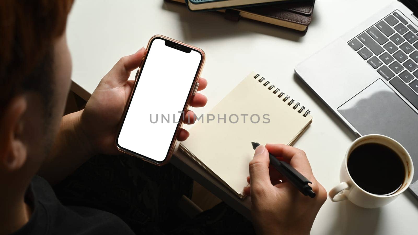 Closeup view of man holding mobile phone and making notes on notepad. Blank screen for advertising text message by prathanchorruangsak