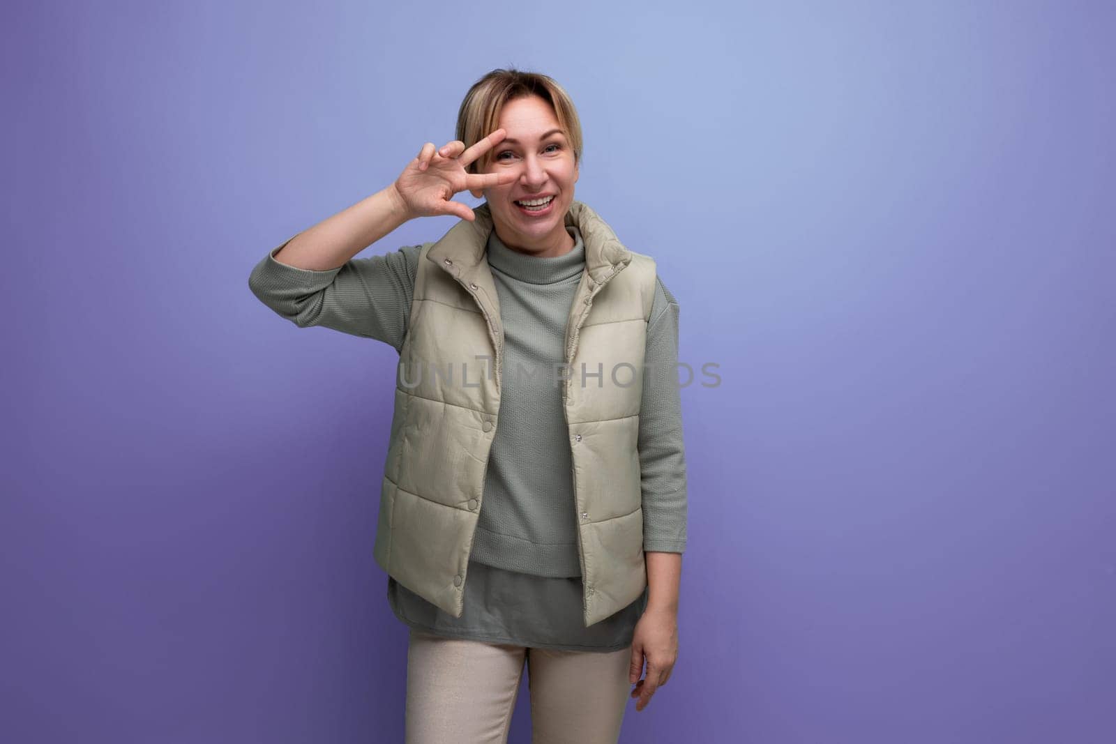 portrait of a cheerful blond young woman in a beige vest on a blue background.