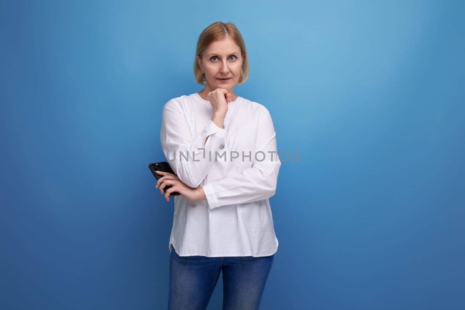 kind pleasant blond mature woman decides where to spend money from the card on a studio background.