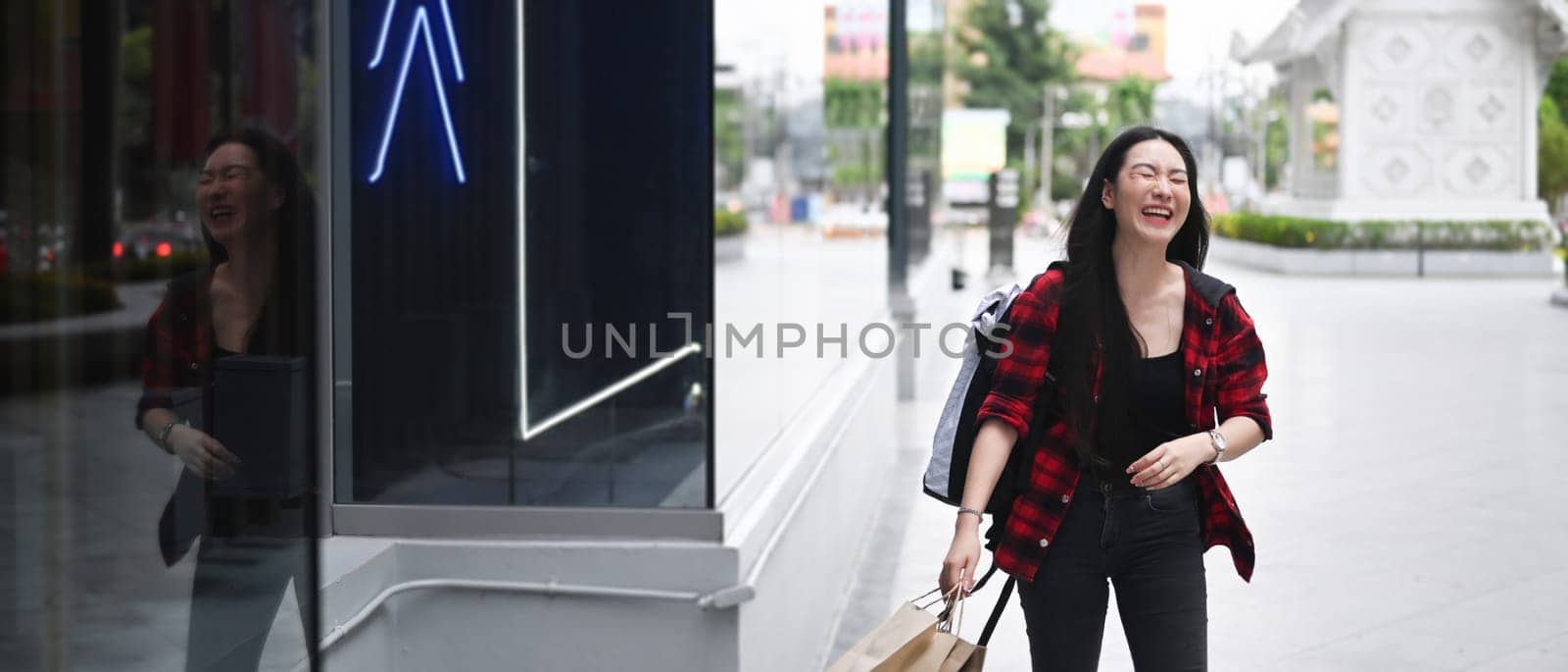 Cheerful Asian woman holding shopping bags and walking in the city street.