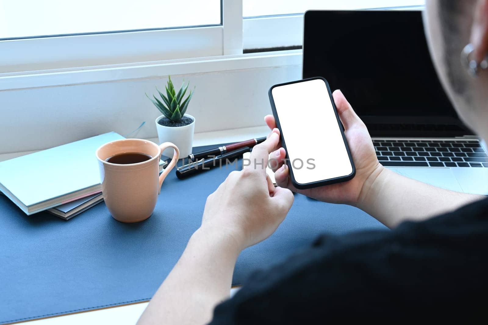 Over the shoulder view of young man sitting at workplace and using smart phone.