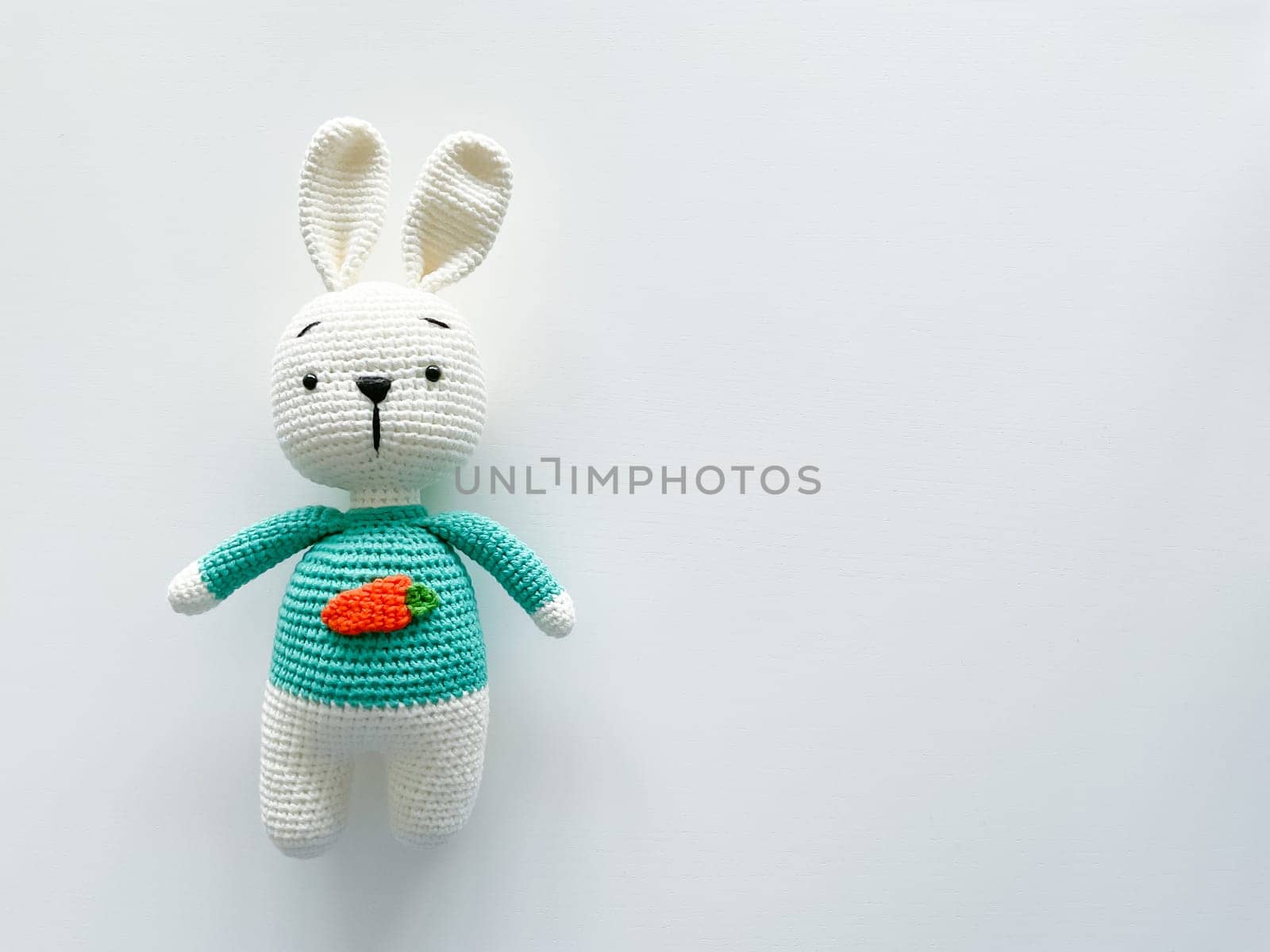 Soft white crochet bunny. on a white background. Handmade children's toy. Large knitted plush rabbit with a carrot on his chest. happy childhood concept