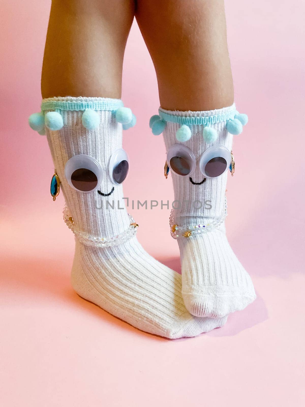 Baby socks with eyes and a smile on a pink background. Cute funny socks with eyes and decorations on the feet of a child.