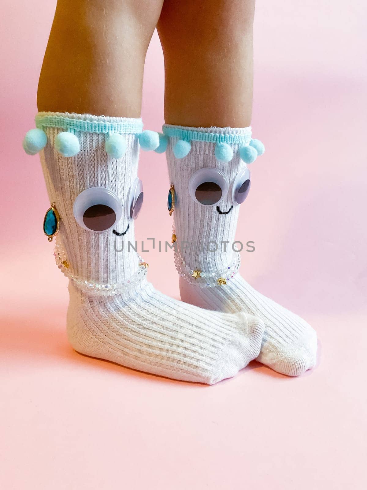 Baby socks with eyes and a smile on a pink background. Cute funny socks with eyes and decorations on the feet of a child.