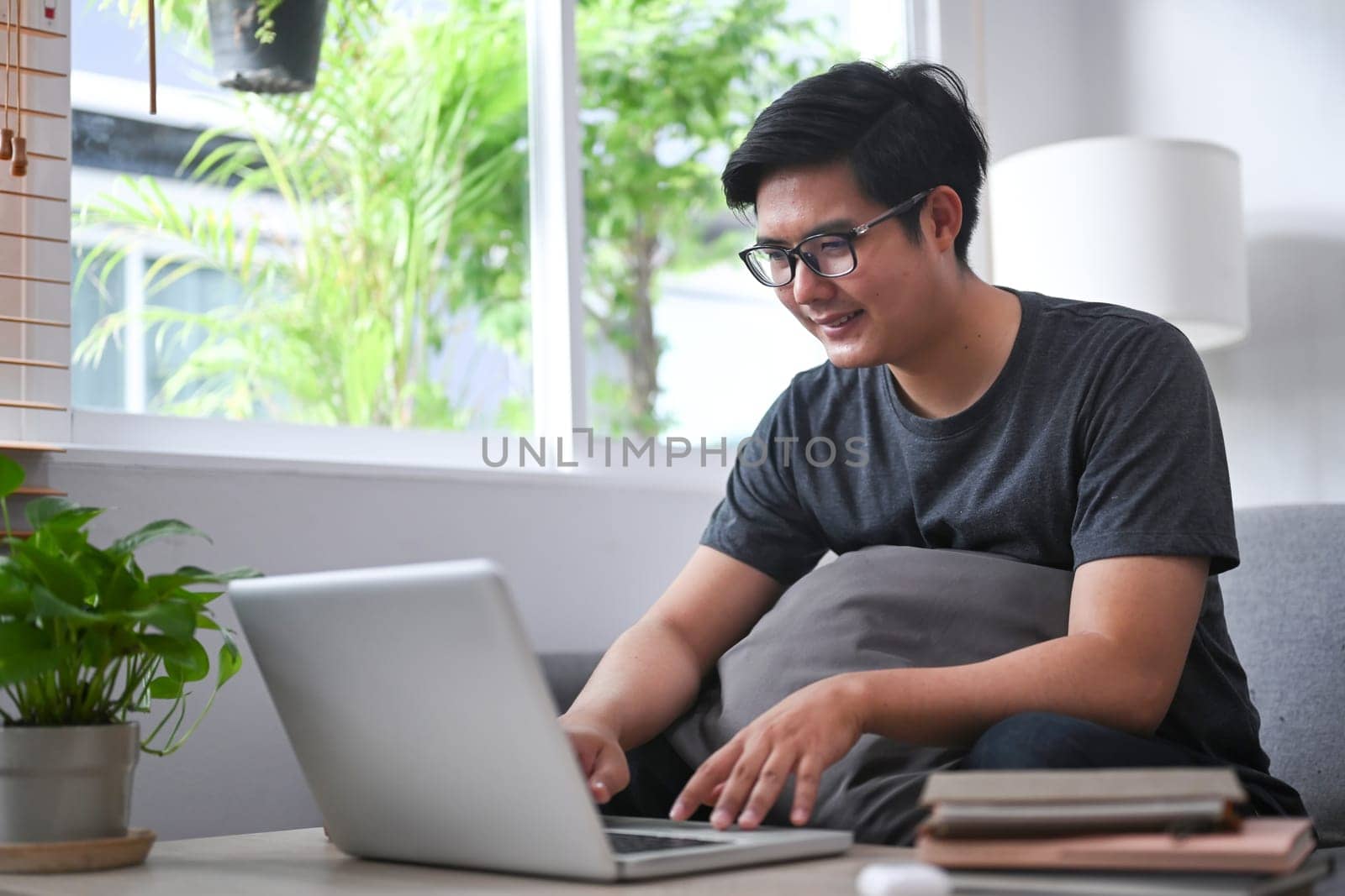 Young Asian man sitting on comfortable sofa and using computer laptop. by prathanchorruangsak
