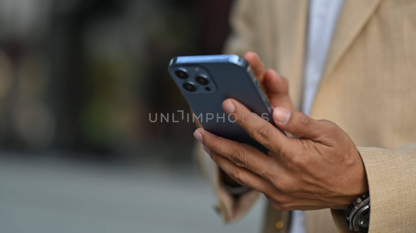 Cropped image of businessman texting messages, chatting in social on smartphone while standing outdoor.