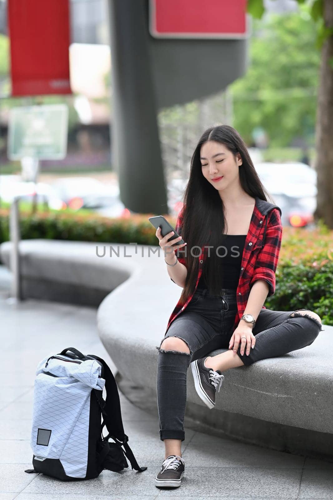 Full length portrait Asian woman sitting at outdoors in city and using smart phone.