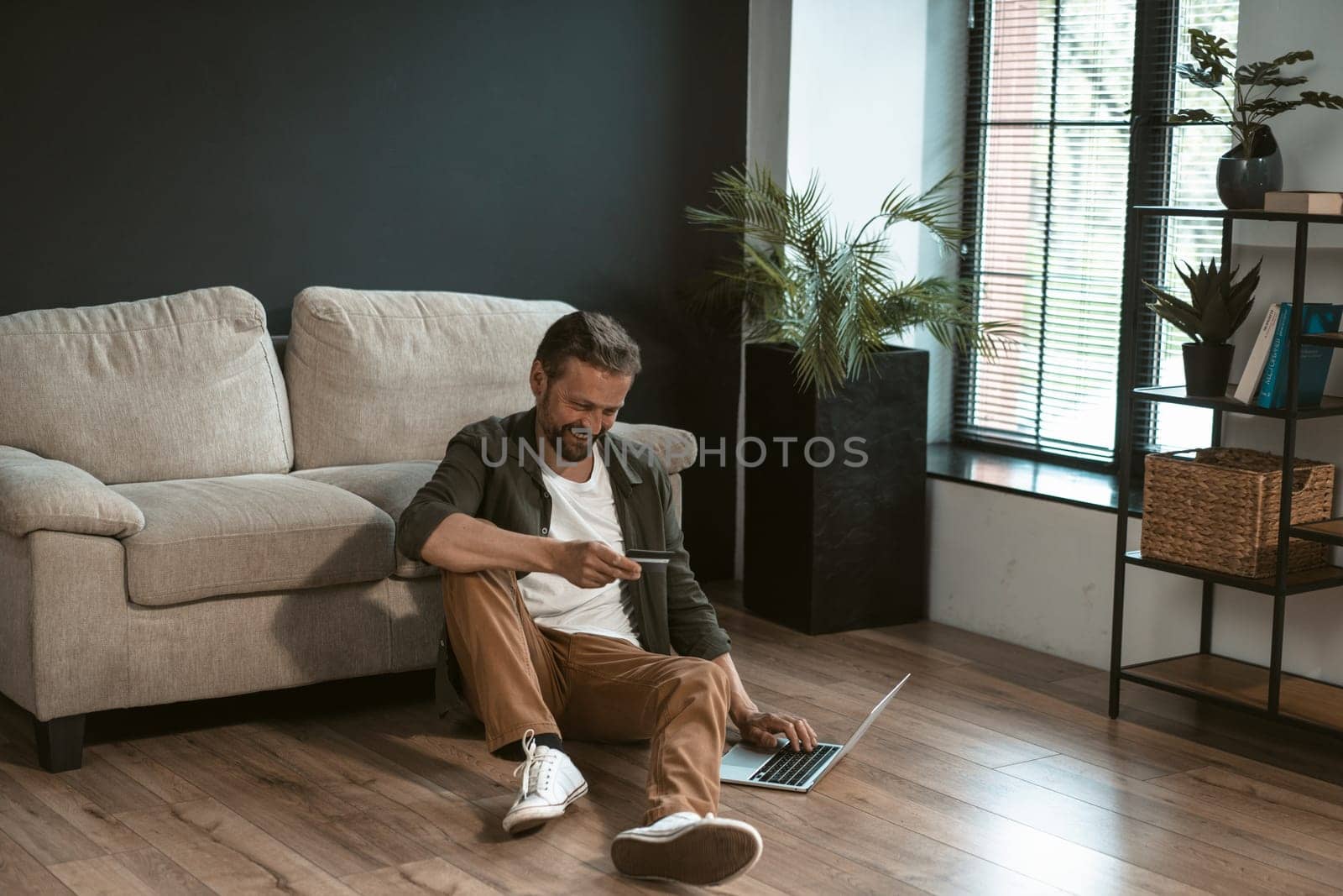 Mid-aged man is holding credit card and using laptop to make online payment. He entering payment information on website, which can not be seen on computer screen. by LipikStockMedia