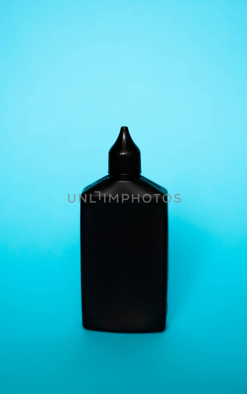 Mock up unbranded black bottle of finish line dry bicycle lubricant with teflon on blue background. Bicycle care, bicycle chain care