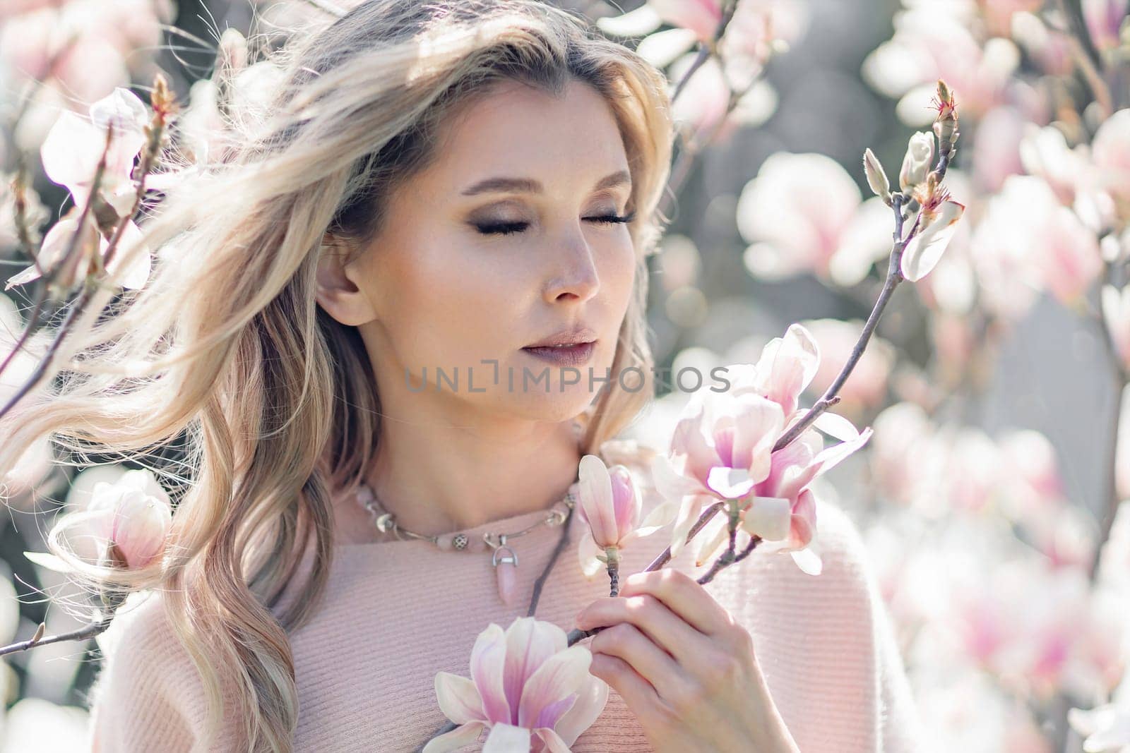 Portrait of a beautiful happy middle aged woman enjoying the smell in a blooming spring garden. Beautiful magnolia bushes, large flowers