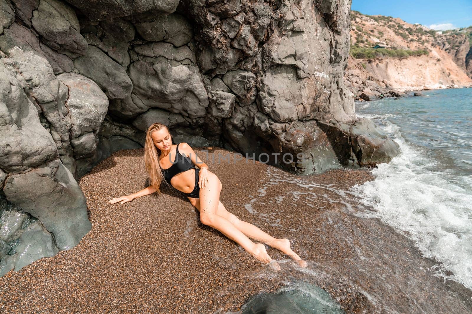 Woman swimsuit sea. Attractive blonde woman in a black swimsuit enjoying the sea air on the seashore around the rocks. Travel and vacation concept