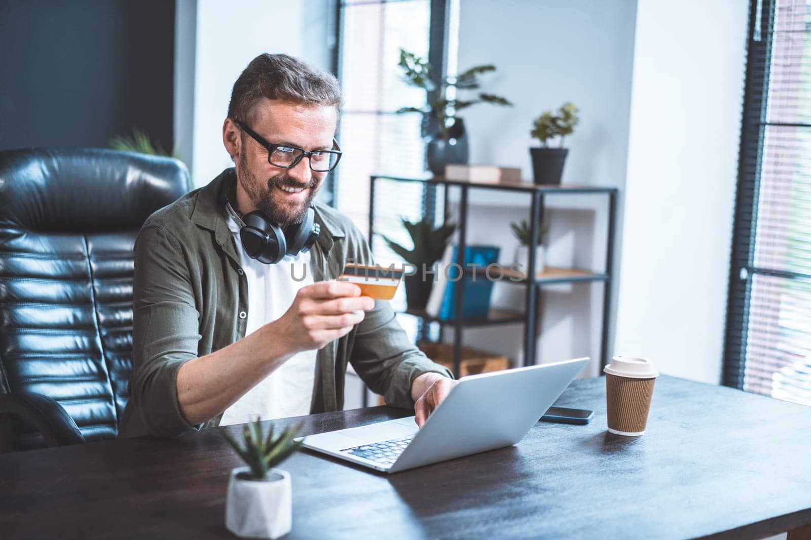 Happy freelancer checking salary online while holding credit card and looking at laptop on payment service website. by LipikStockMedia