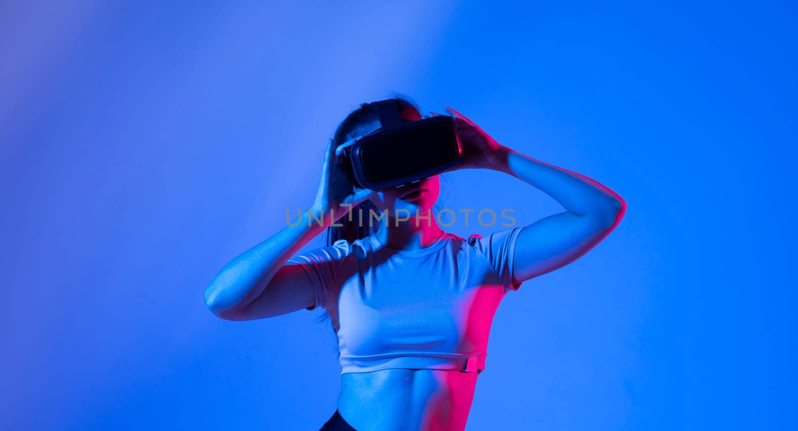 Young brunette woman wearing virtual reality device, vr glasses and playing a game with a friends online in neon light