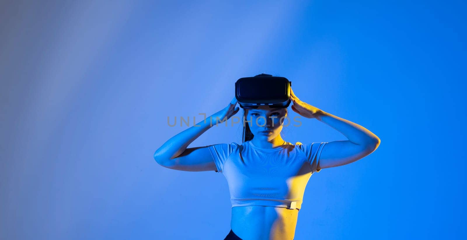 Young woman wearing virtual reality goggles and speasing with a friends in the metaverse. Famale in a black top exploring virtual reality video games in a studio