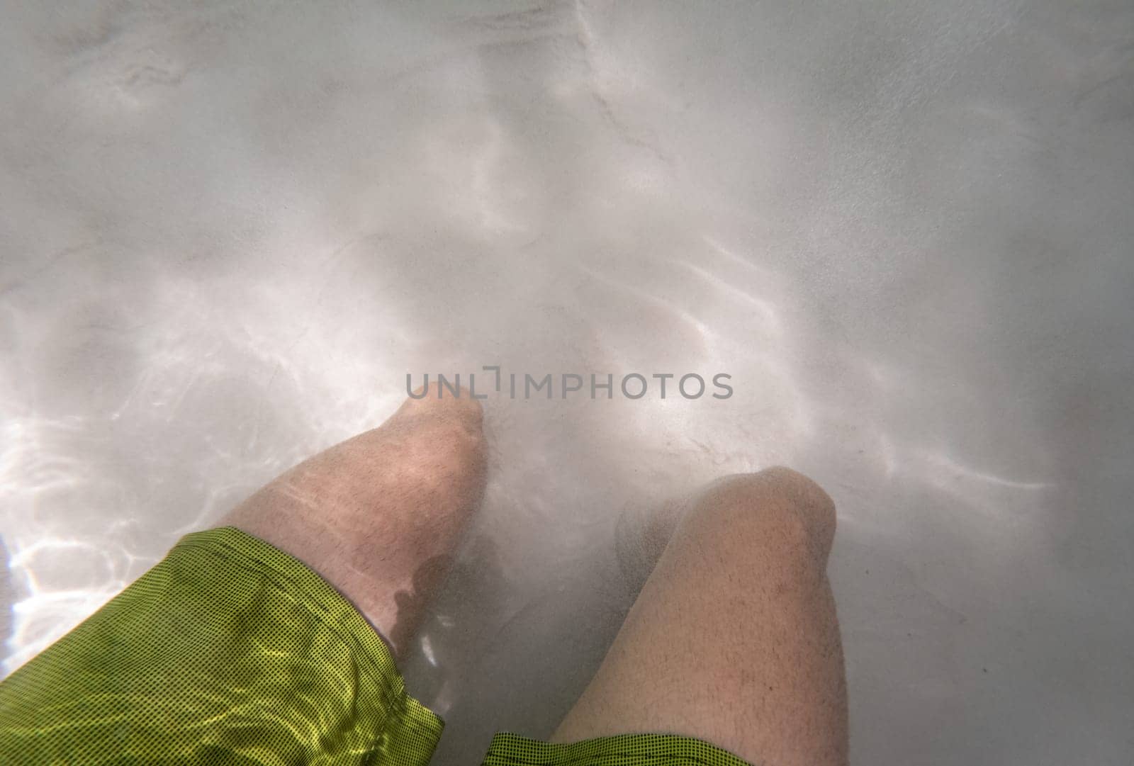 A pair of legs in a bathing suit sink into the sand of a fervedouro in Jalapao, disappearing underwater.