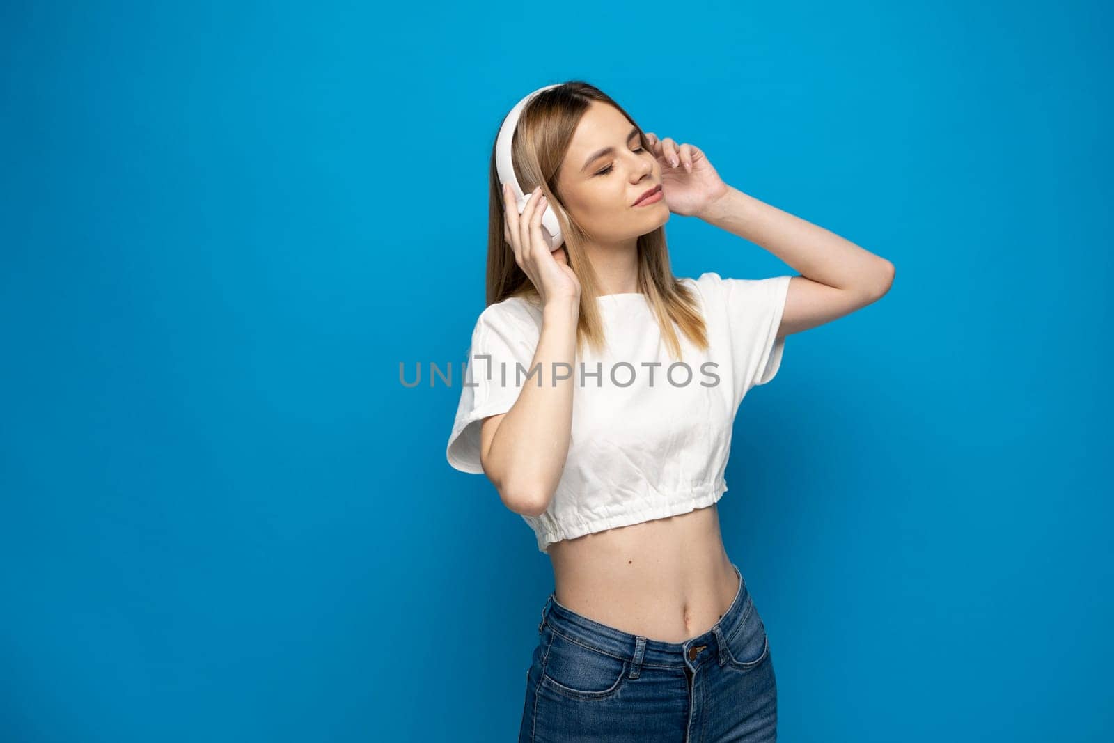 Portraite of lovely cheerful girl listening music isolated over bright blue color background