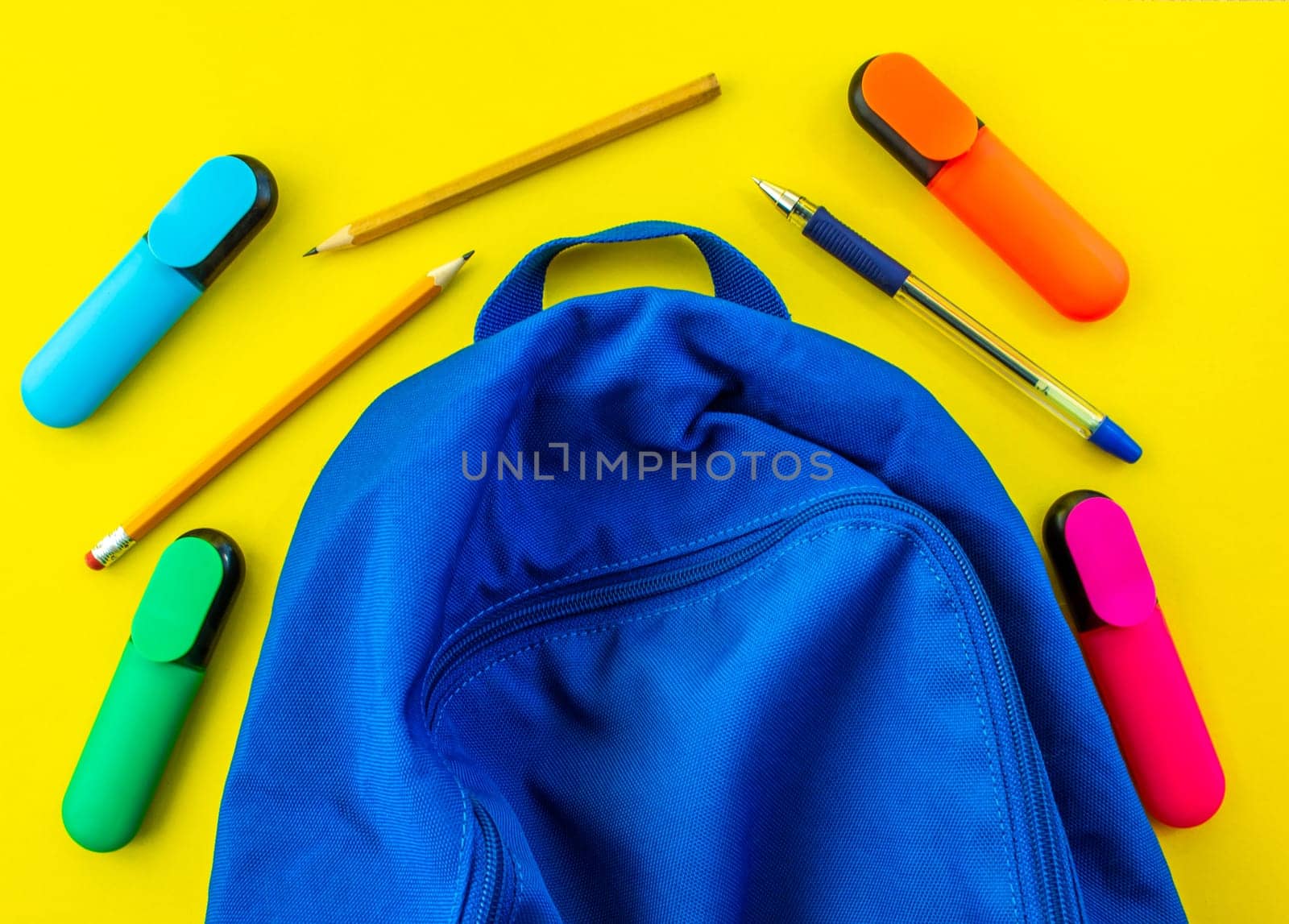 School backpack, pencils, markers and a pen on a yellow background. School blue backpack, pencils, markers and a pen on a yellow background.