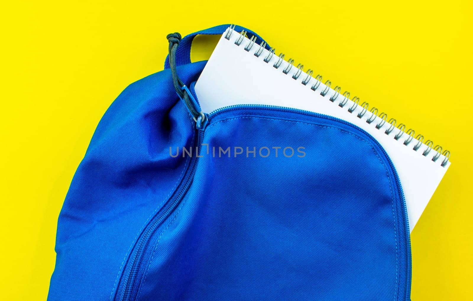 School backpack and notebook on a yellow background. School blue backpack with a notepad inside on a yellow background.