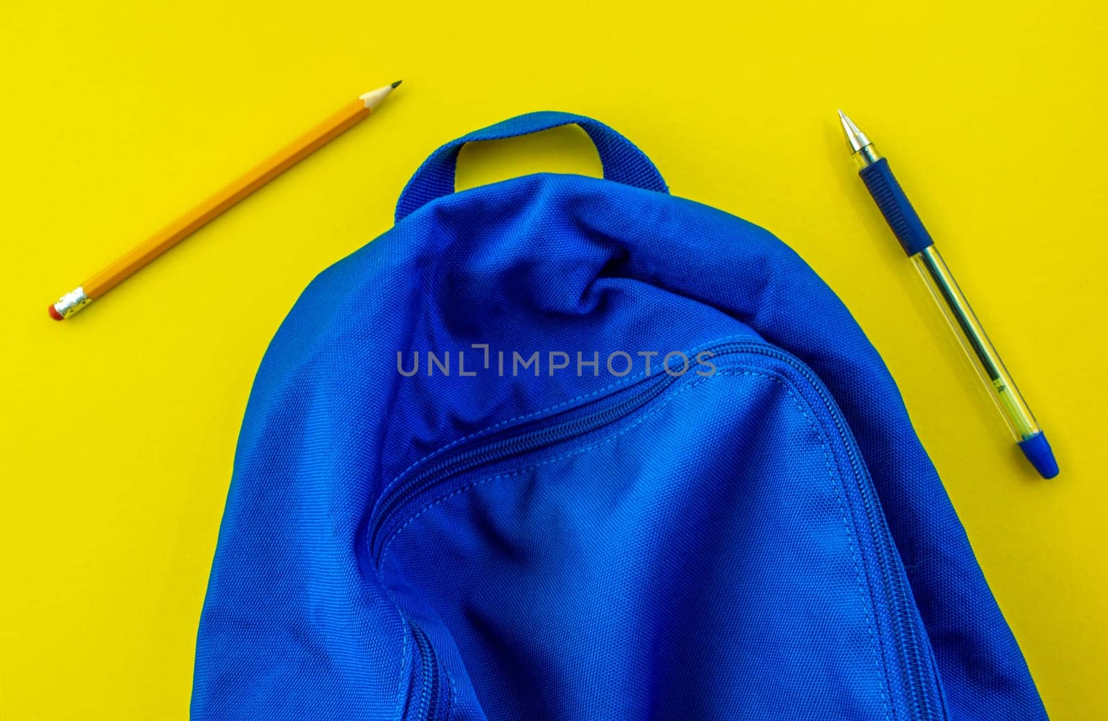 School backpack, pencil, pen on a yellow background. School blue backpack, pencil and pen on a yellow background.