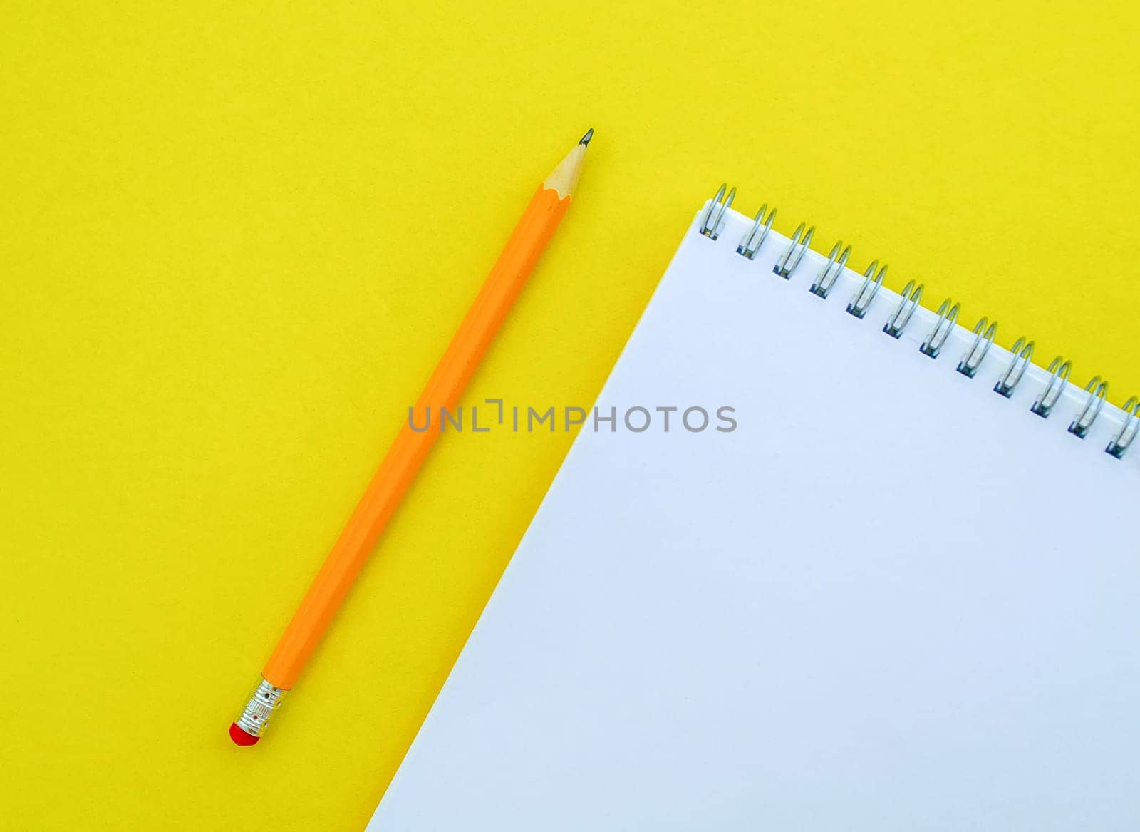 White notebook with a spring and a pencil. School white notebook and pencil on a yellow background.