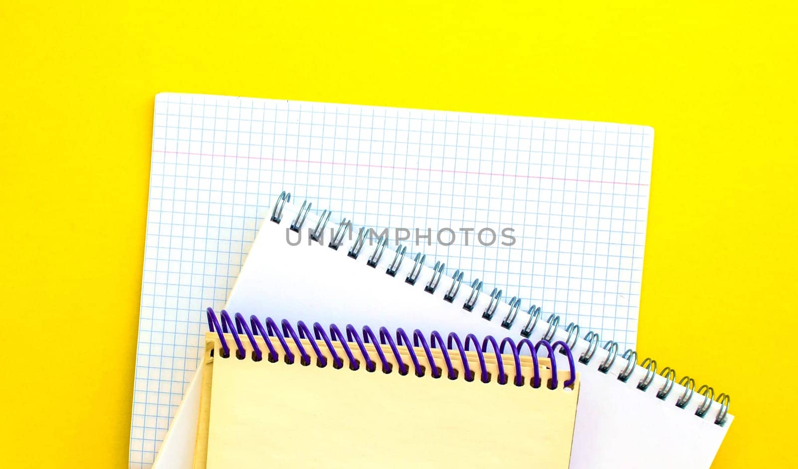 White and beige notepads and a checkered notebook on a yellow background. School white and beige notebooks and a checkered notebook on a yellow background.