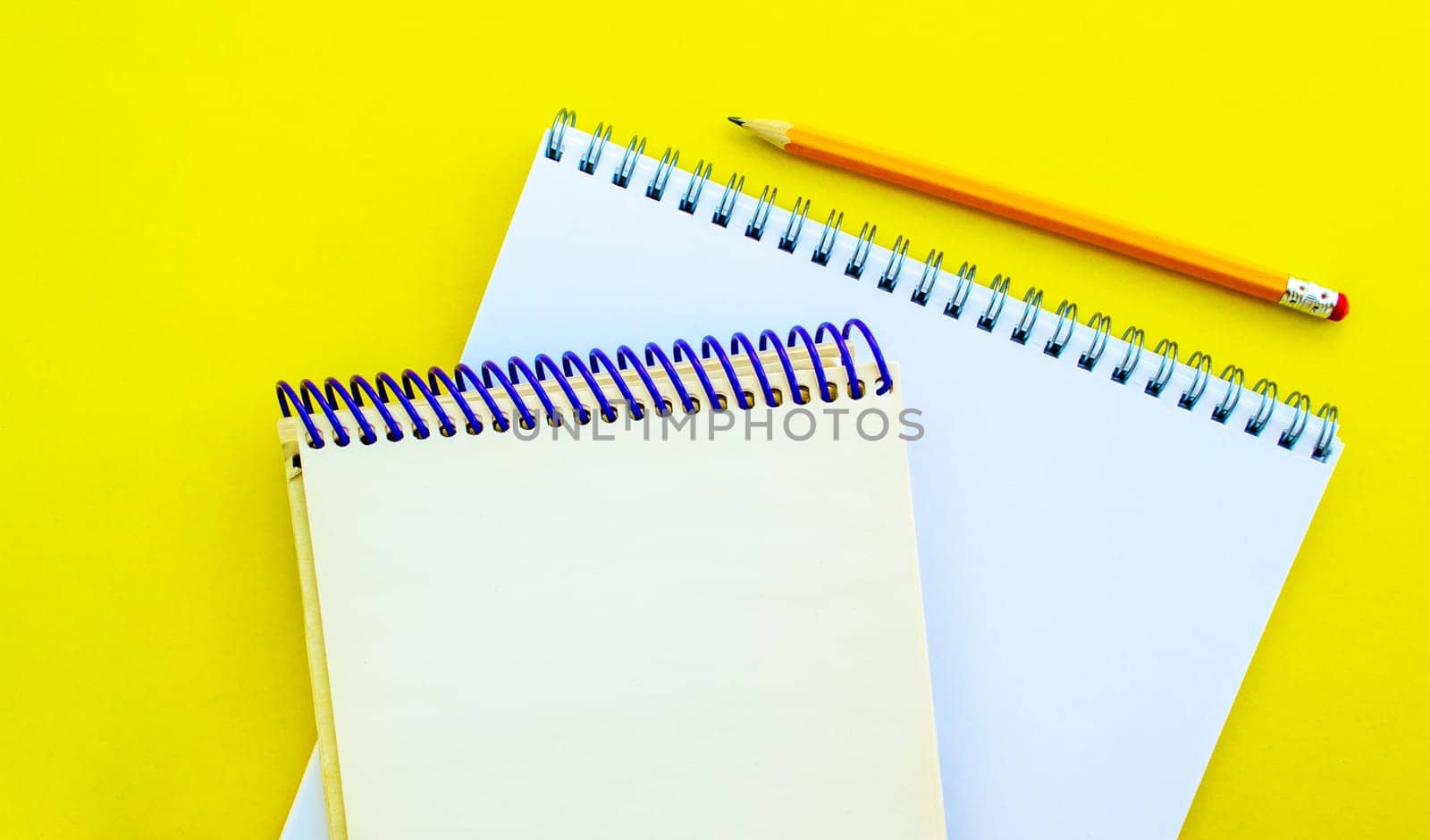 White and beige notepads and a pencil on a yellow background. School white and beige notebooks and a pencil on a yellow background.