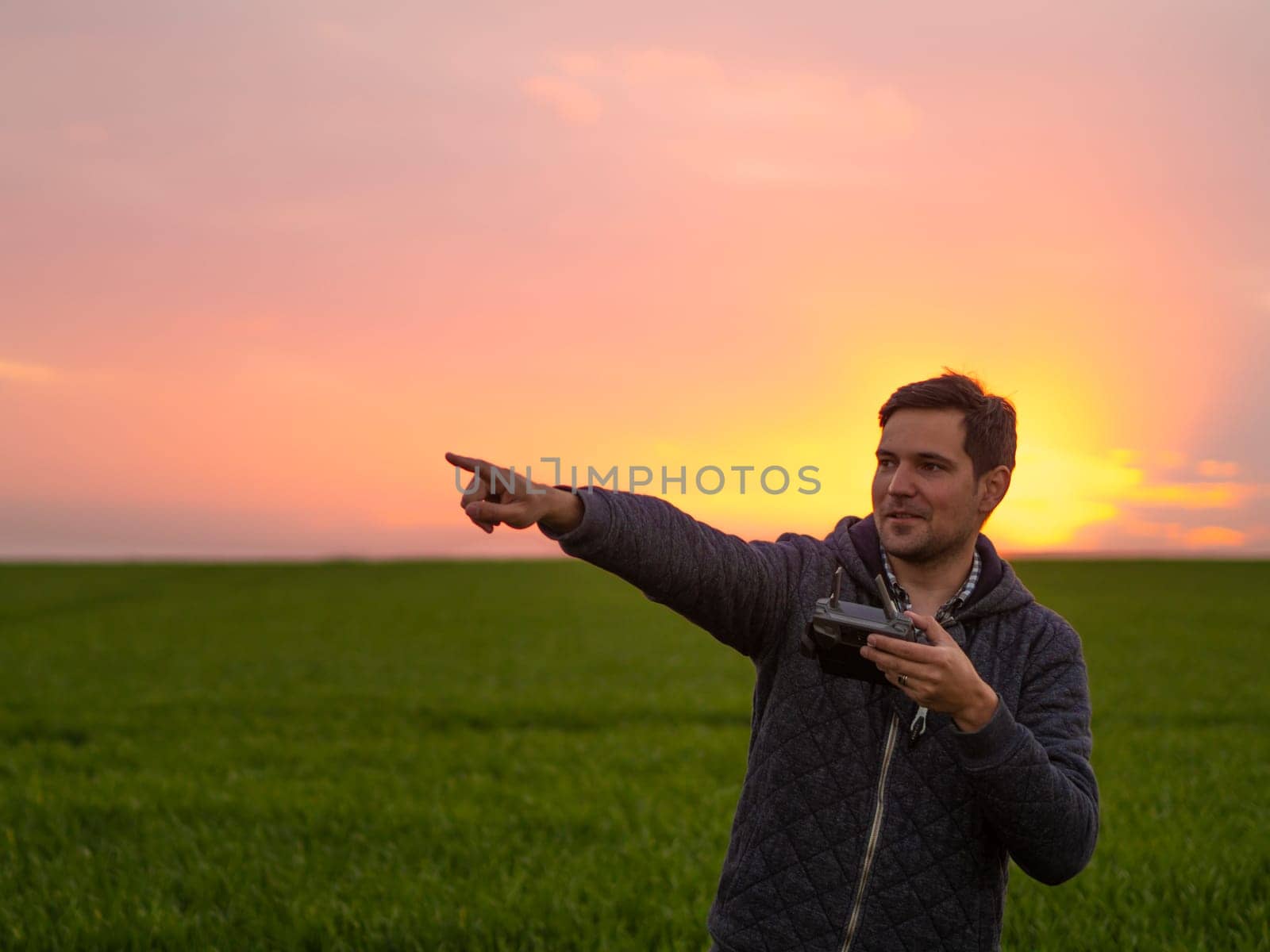 Man portrait operating the drone by remote control at sunset magic golden hour. Filming night landscape