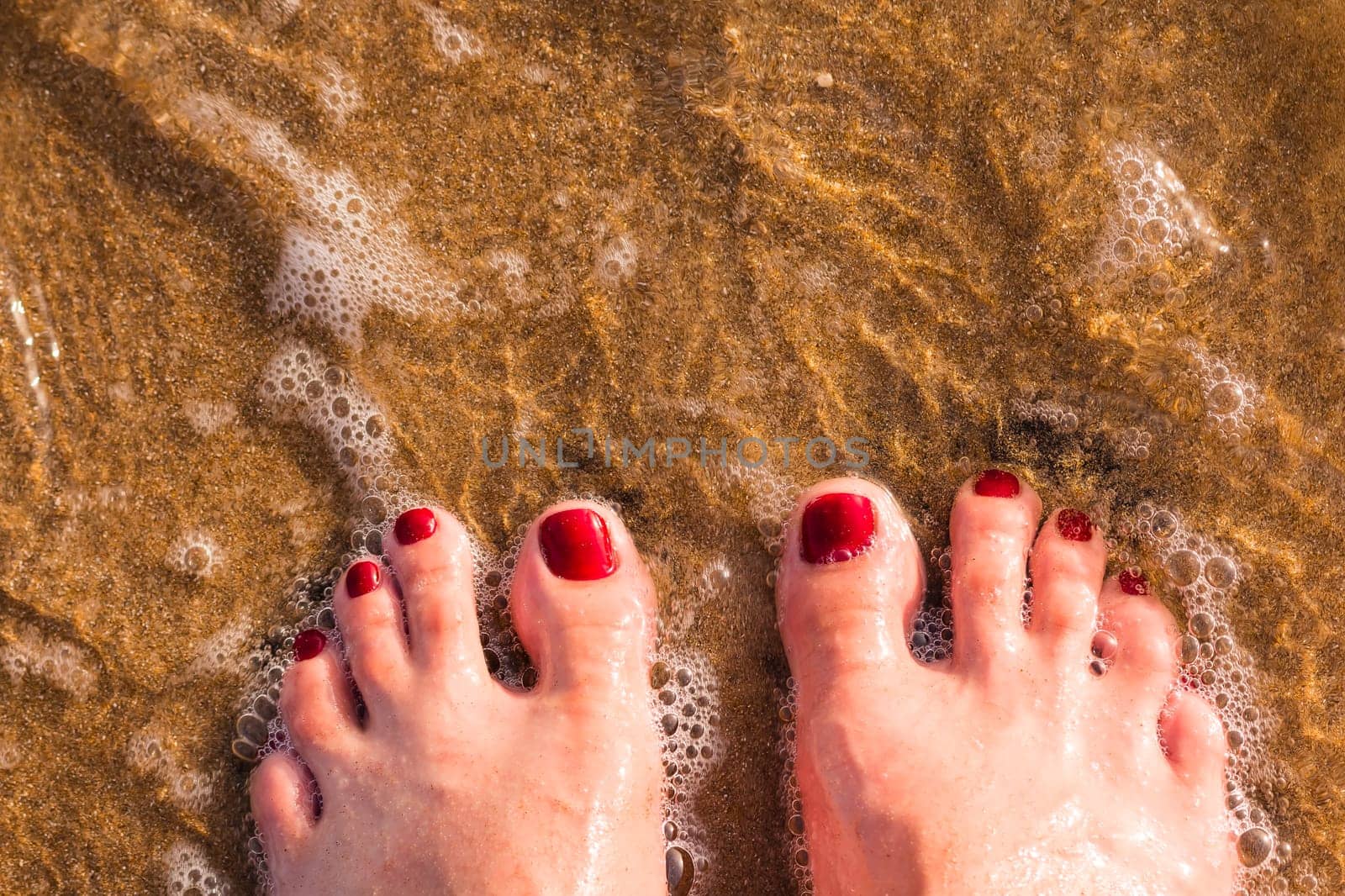 Woman's legs wear jeans with bare feet stand on sand at beach, hello summer.Girl bare foot relaxing in clear water