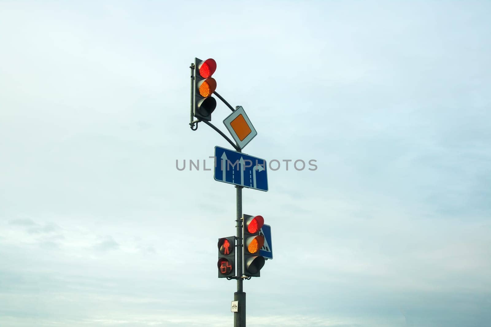 Red traffic light and road signs against the sky close up