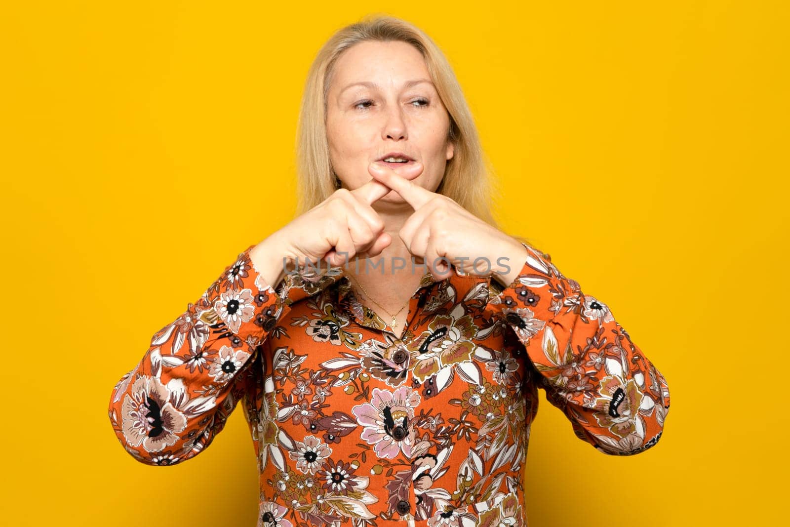 Caucasian blonde woman wearing a patterned sweater over a yellow background has an angry expression of rejection crossing her fingers making a negative sign.