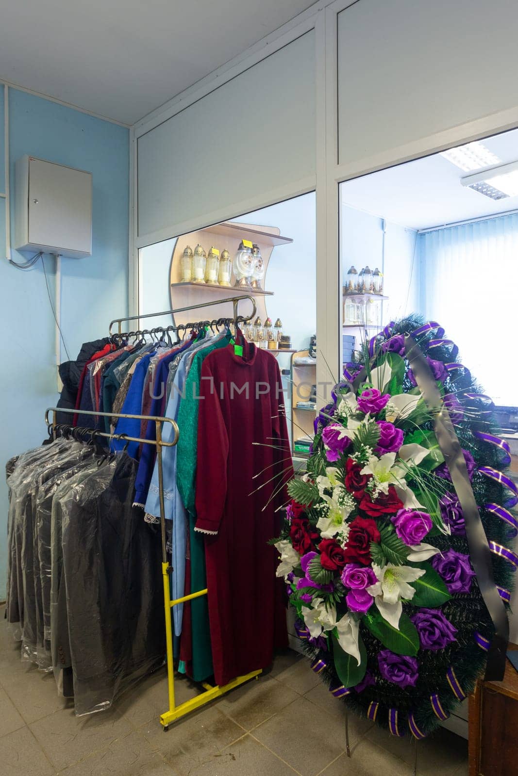 Hangers with men suits and women clothes for the deceased in a funeral goods store. by BY-_-BY