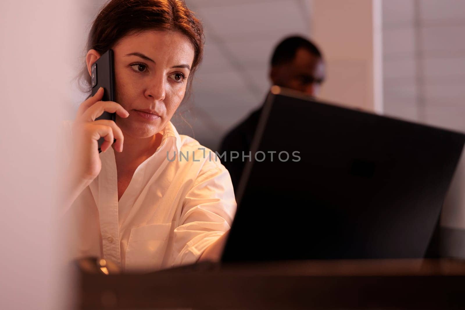 Employee discussing report on smartphone, checking data on website, working on laptop in office. Woman answering mobile call, financial analyst having telephone communication