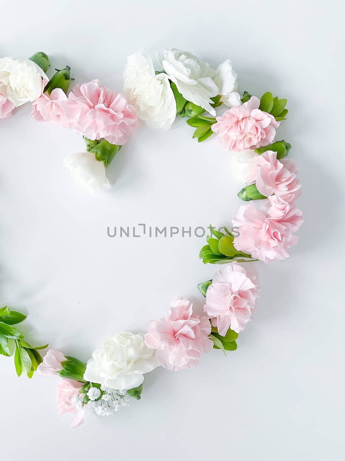 Frame in the form of a heart from pink and white carnations, green leaves, gypsophila on a white background. Flat lay, top view. Spring background. Suitable for wedding, cards and invitations
