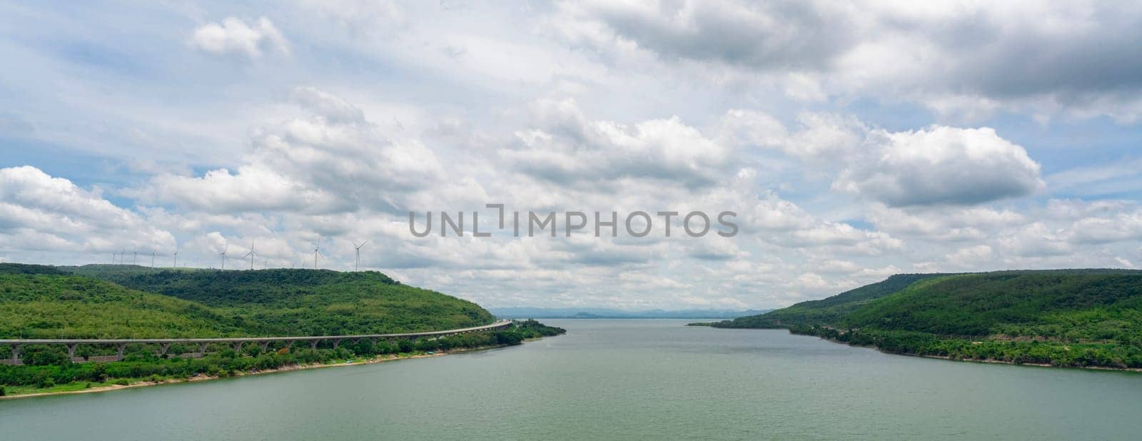 Landscape green mountain with wind turbine farm and water reservoir with blue sky and white clouds. Wind energy. Wind power. Sustainable, renewable energy. Green technology. Sustainable development. by Fahroni