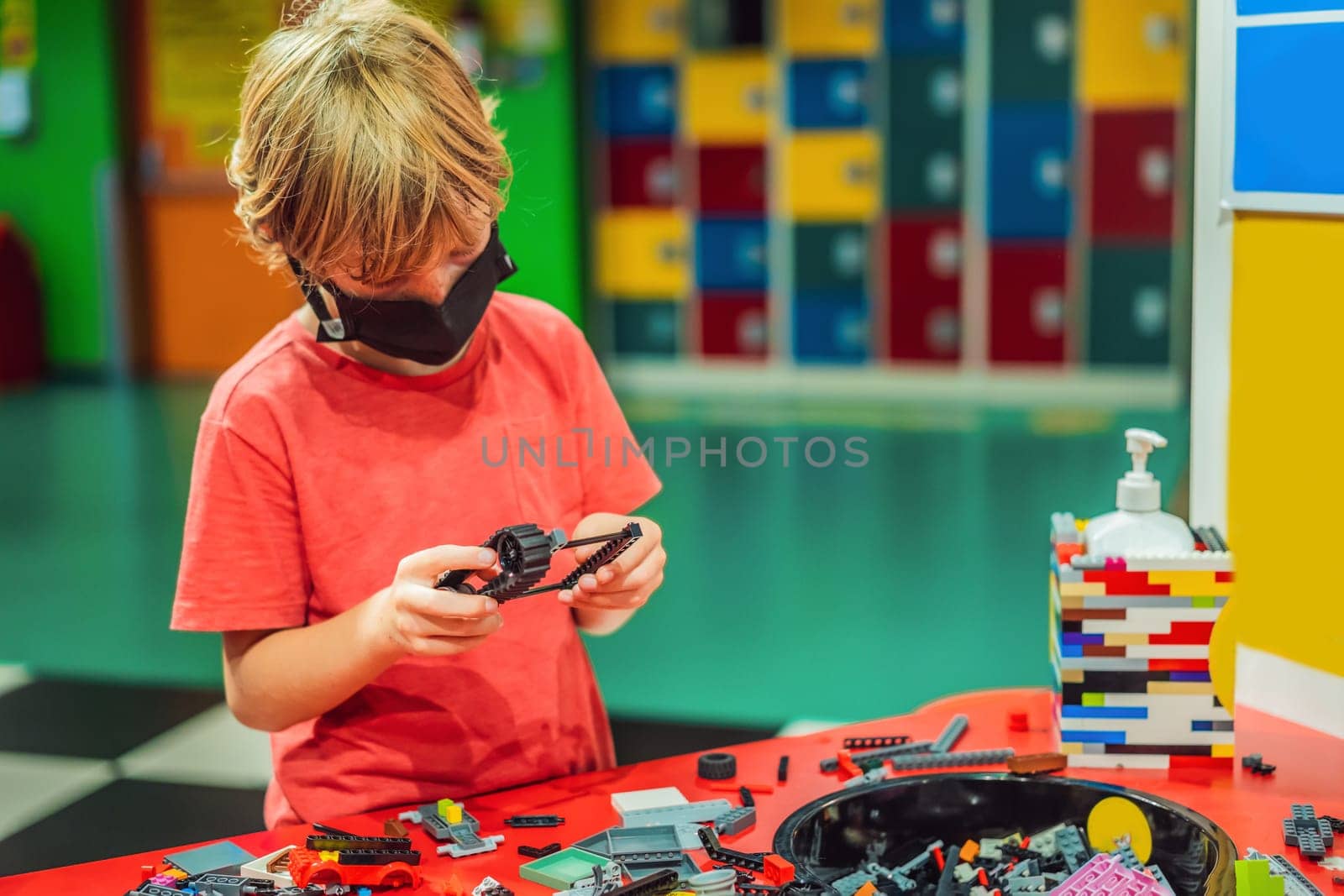 A boy in a medical mask plays with a constructor. child playing and building with colorful plastic bricks table. Early learning and development.