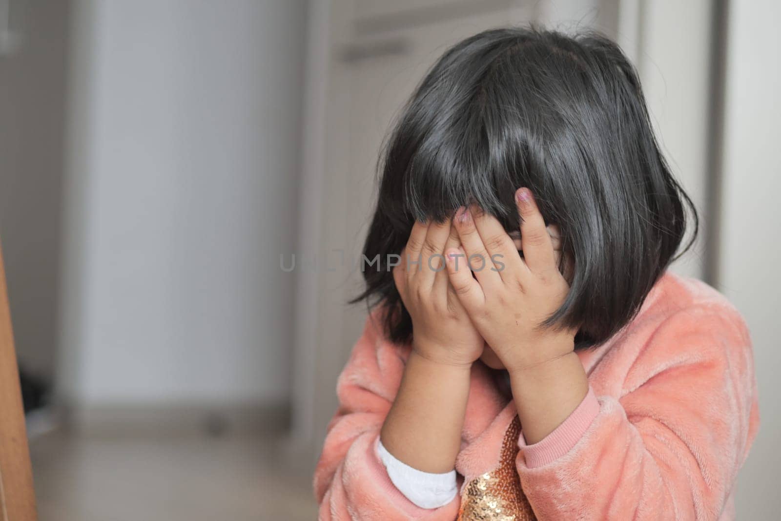 a upset child girl cover her face with hand .