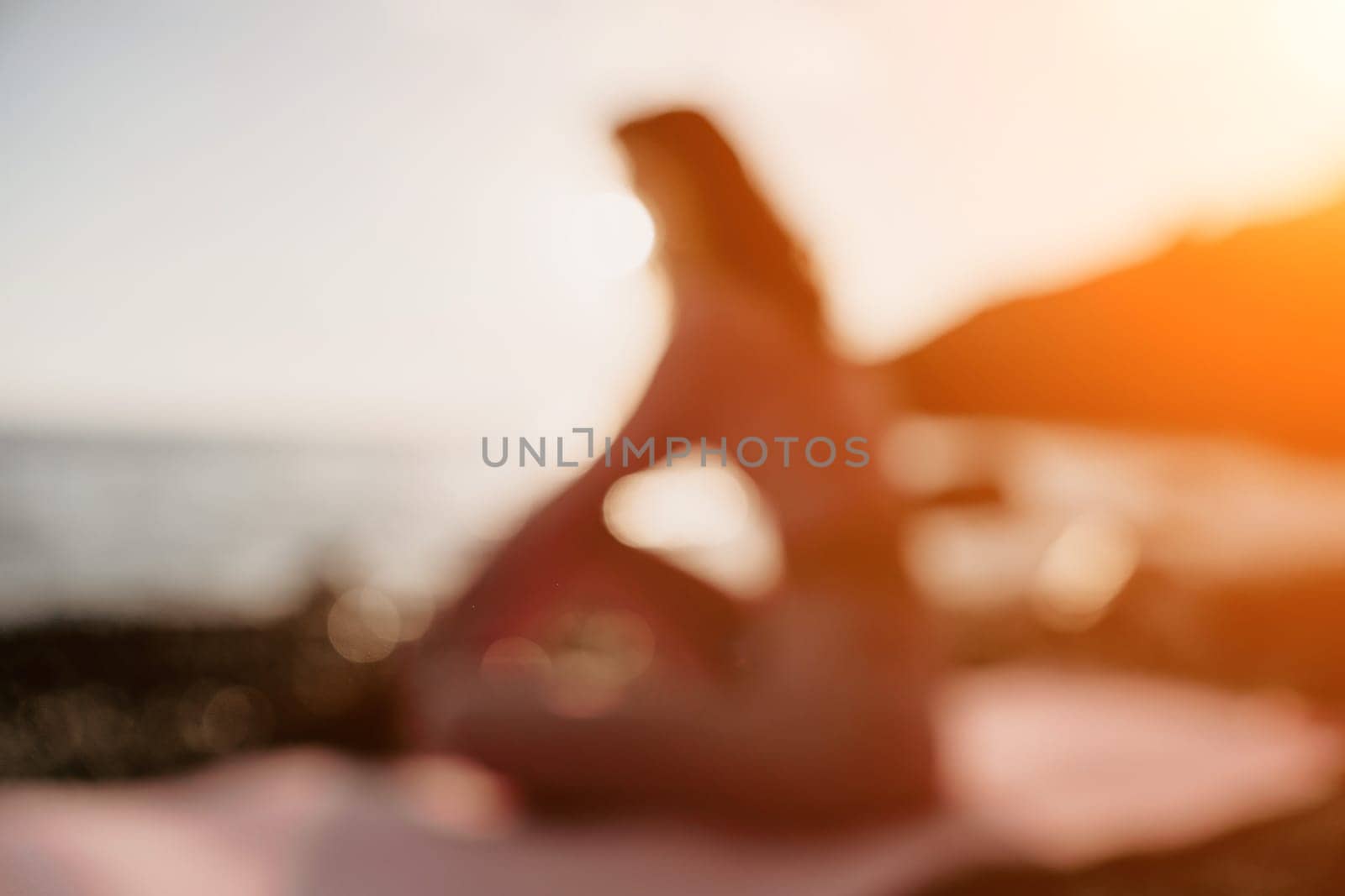 Young woman with black hair, fitness instructor in pink sports leggings and tops, doing pilates on yoga mat with magic pilates ring by the sea on the beach. Female fitness daily yoga concept