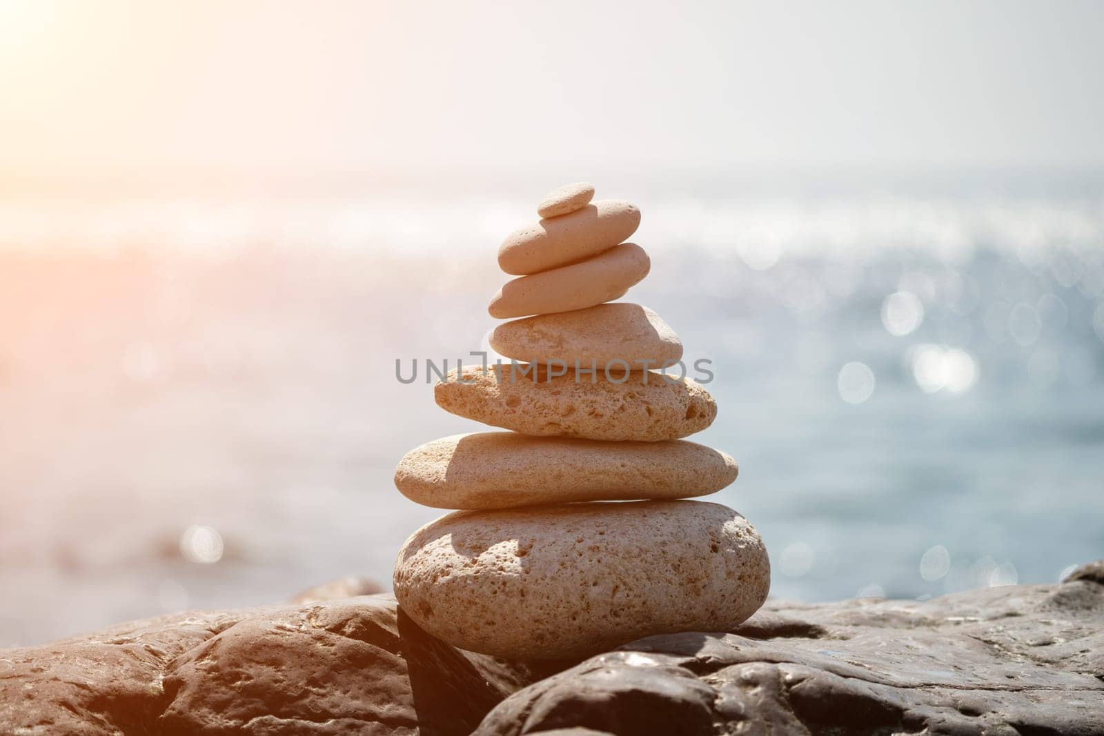 Balanced Pebbles Pyramid on the Beach on Sunny Day and Clear Sky at Sunset. Blue Sea on Background Selective focus, zen stones on sea beach, meditation, spa, harmony, calm, balance concept.