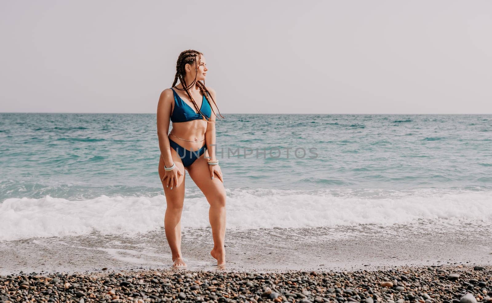 Beach vacation. Hot beautiful woman in sunhat and bikini standing with her arms raised to her head enjoying looking view of beach ocean on hot summer day.