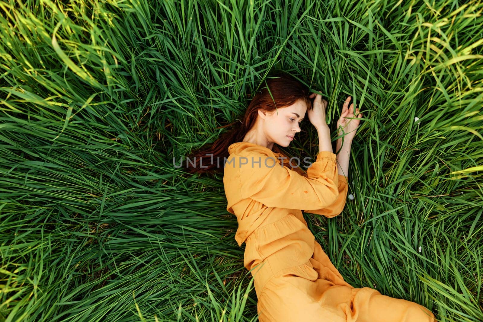 a relaxed woman enjoys summer lying in the tall green grass with her eyes closed. Photo taken from above by Vichizh