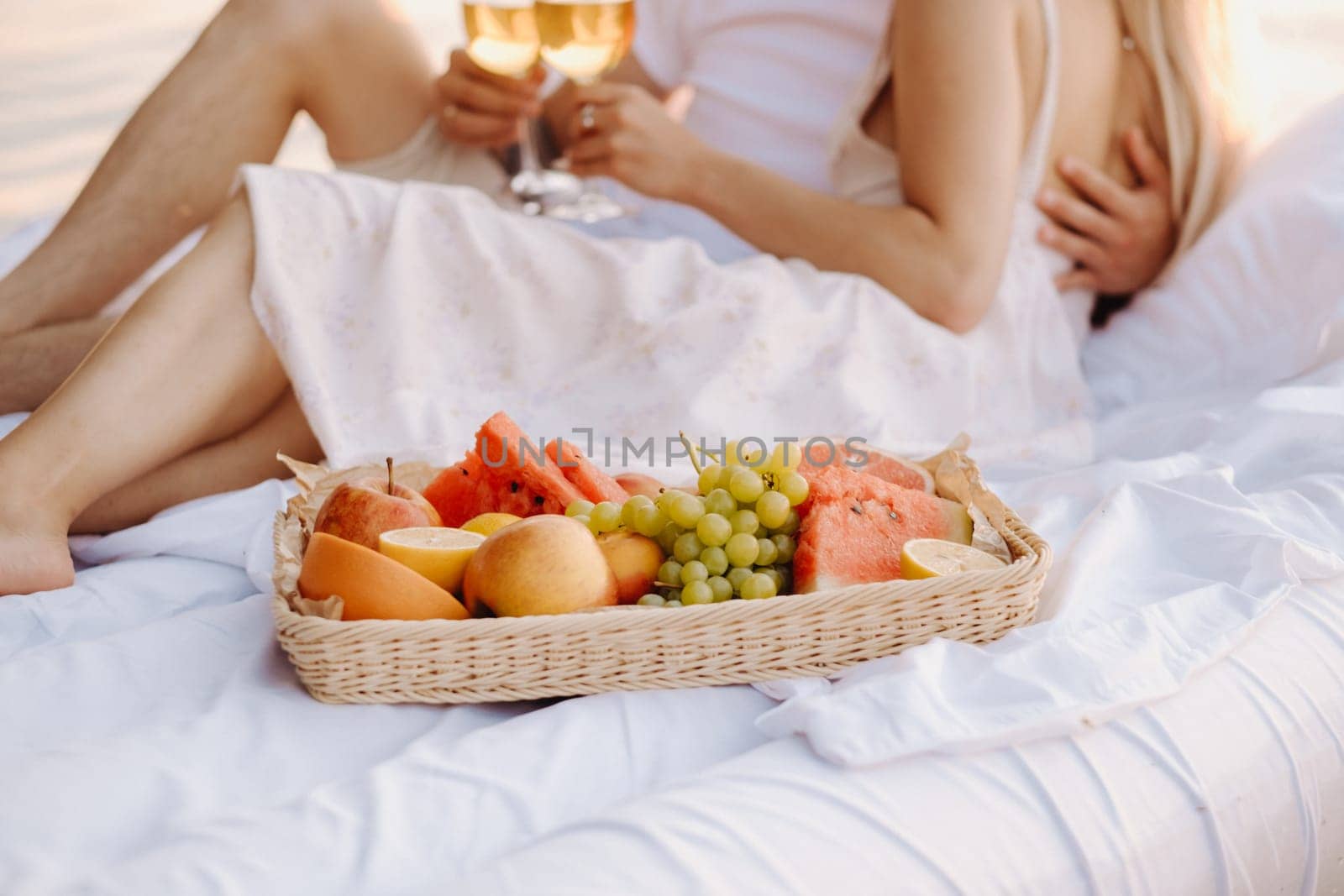 Assorted fruits in a tray on the background of a couple with glasses of wine at sunset.