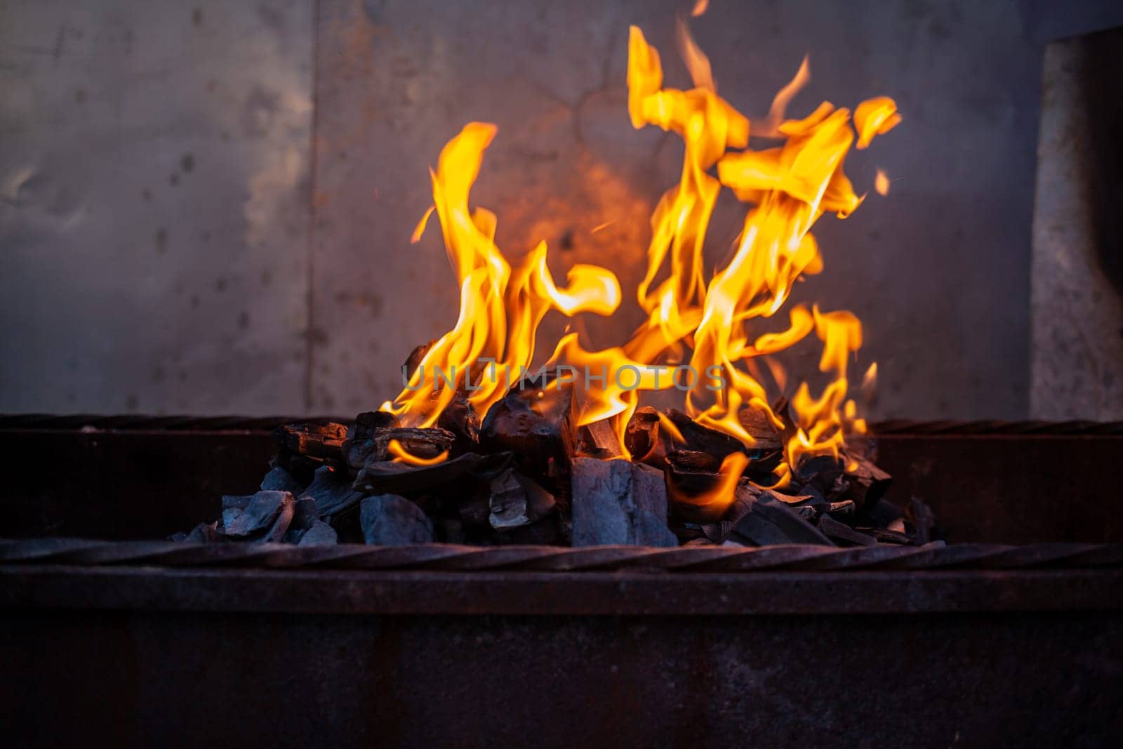 The firewood in the grill burns with a bright orange flame. Preparation for cooking meat on the grill in nature. Fire flames and smoke