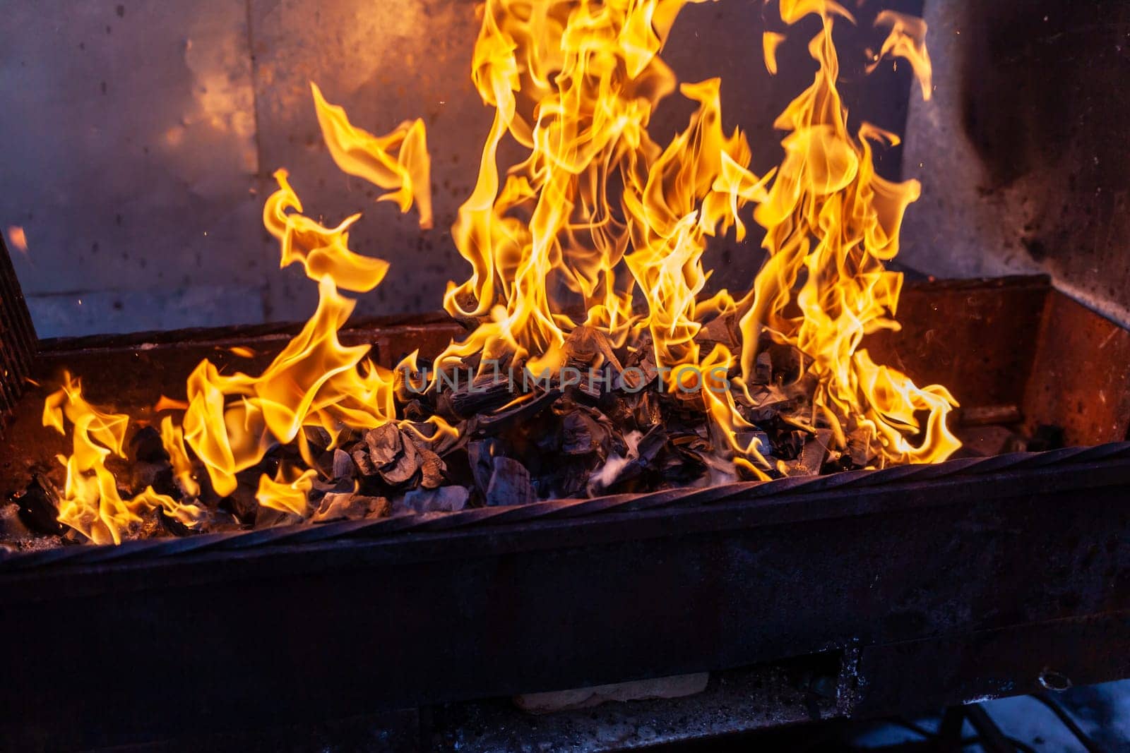 The firewood in the grill burns with a bright orange flame. Preparation for cooking meat on the grill in nature. Fire flames and smoke