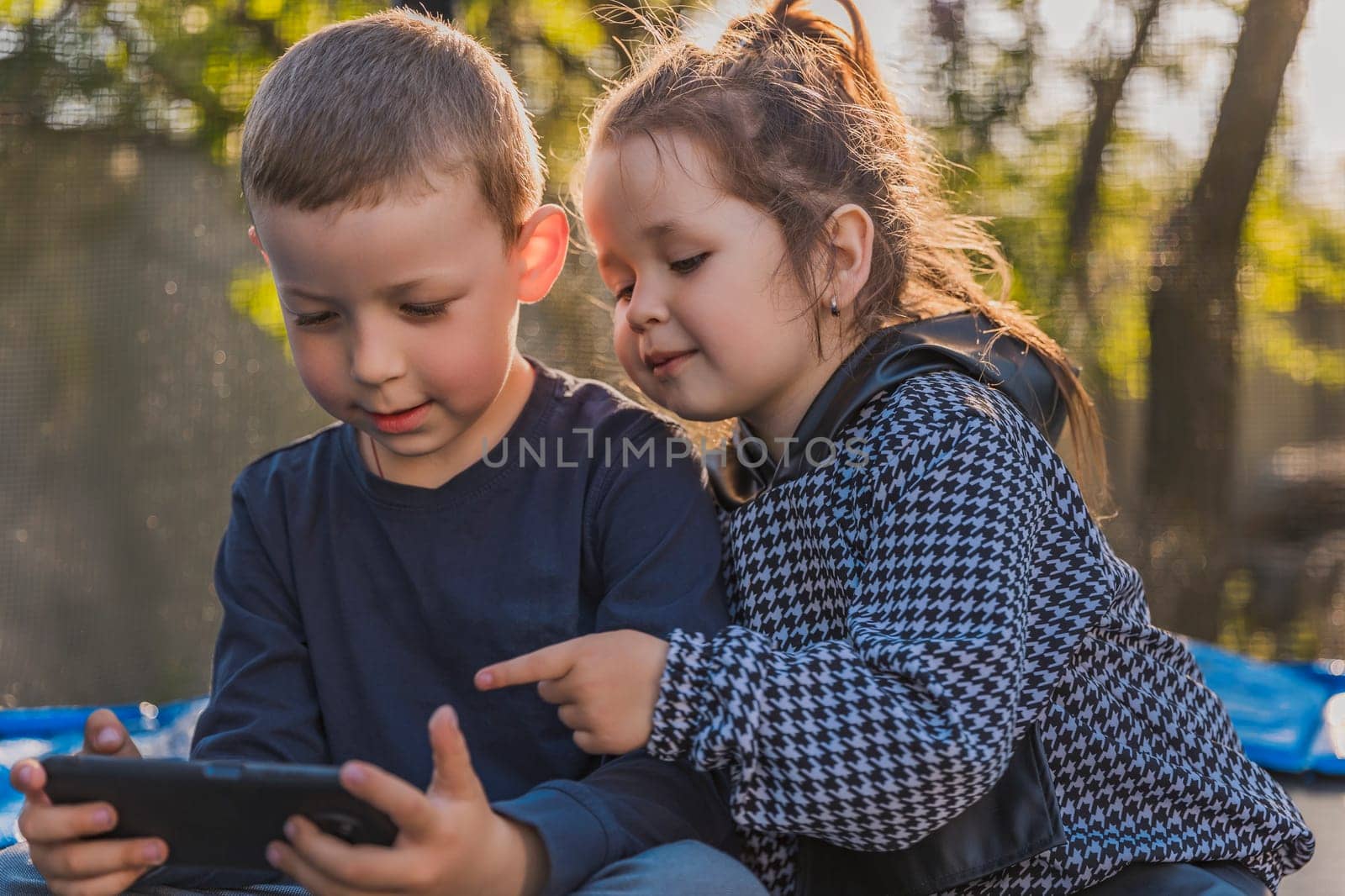 portrait of children who sit on a trampoline and look at the phone