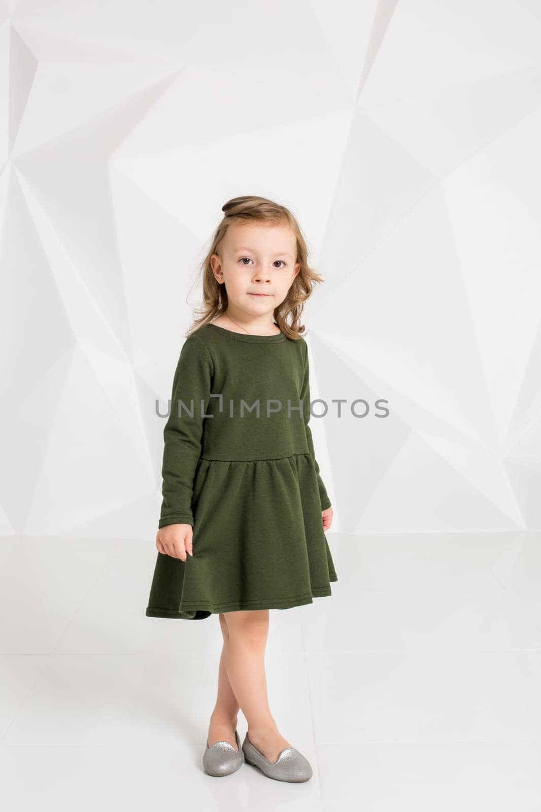 Beautiful little fashion model on white studio background. Portrait of cute girl posing in studio. Little blonde in dark green dress