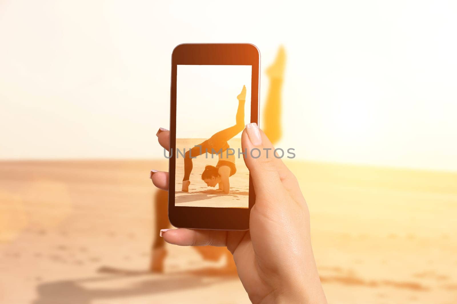 Woman taking a picture with your mobile phone a one woman doing acrobatic stunt on sand by nazarovsergey