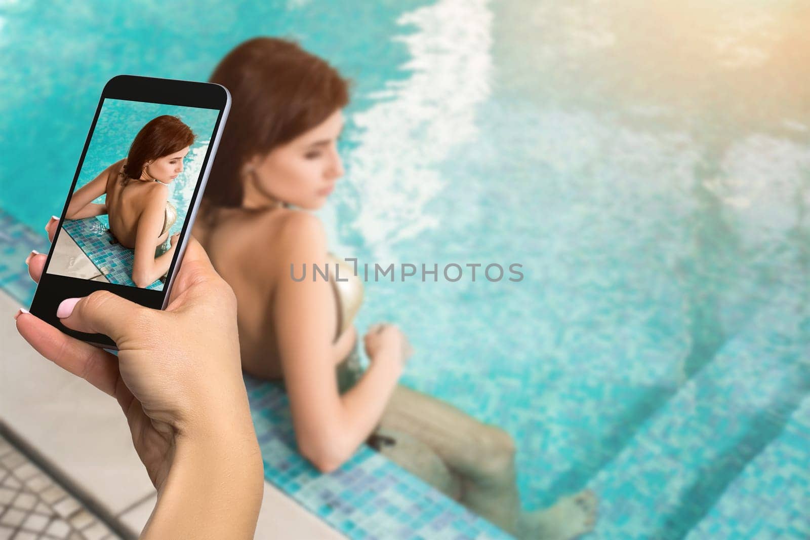 Closely image of female hands holding mobile phone with photo camera mode on the screen. Cropped image of beautiful long hair female model posing by the pool by nazarovsergey