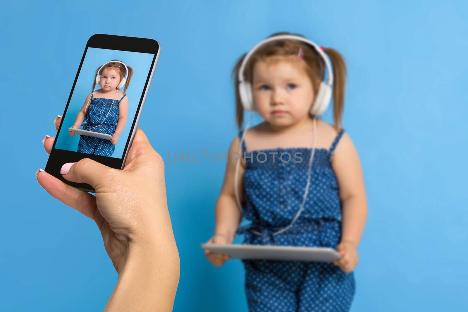 Woman's hand making photo of a little girl with a mobile phone. Selective focus on a mobile phone with a portrait of a girl. Made for social networks