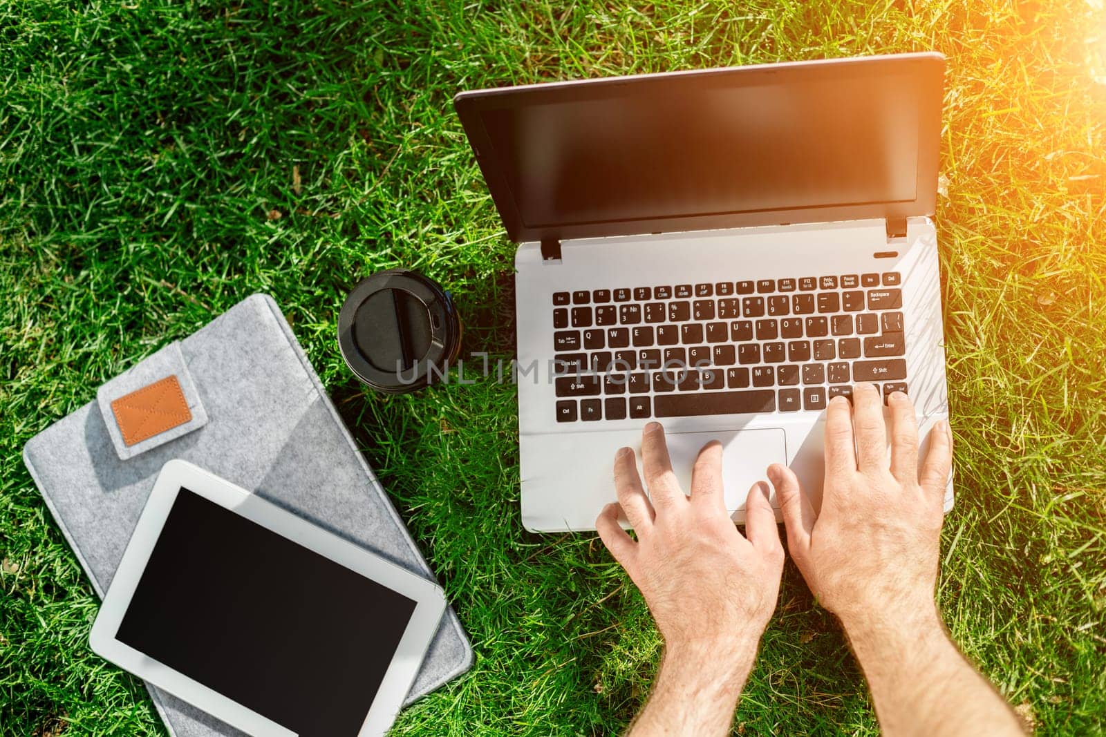 Close-up shot of handsome man's hands touching laptop computer's screen. Businessman using a laptop computer and sitting on the ground. Sun flare